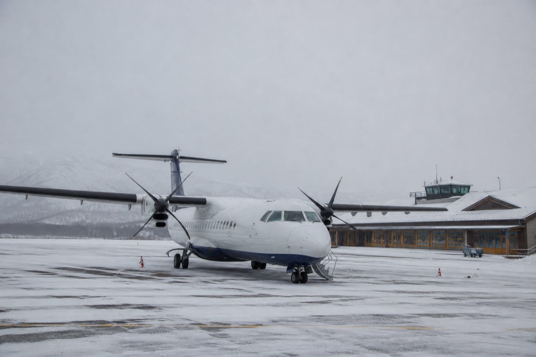 Regional propeller aircraft parked on a snowy apron with a small terminal behind