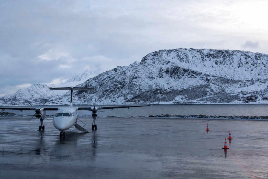 Small regional aircraft on an apron beside snow-covered hills at a northern Norwegian airport