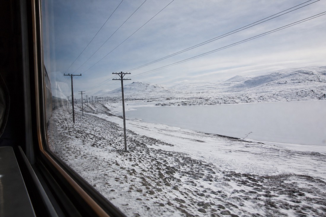 Train window view of a snowy high plateau with a frozen lake and telegraph poles