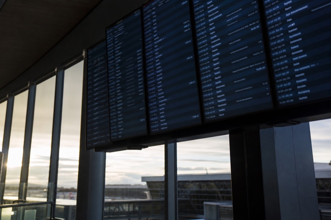 Departure board in a Nordic airport terminal with early morning light through tall windows