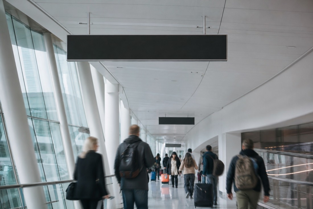 Airport transit corridor with directional signage and travellers walking with luggage