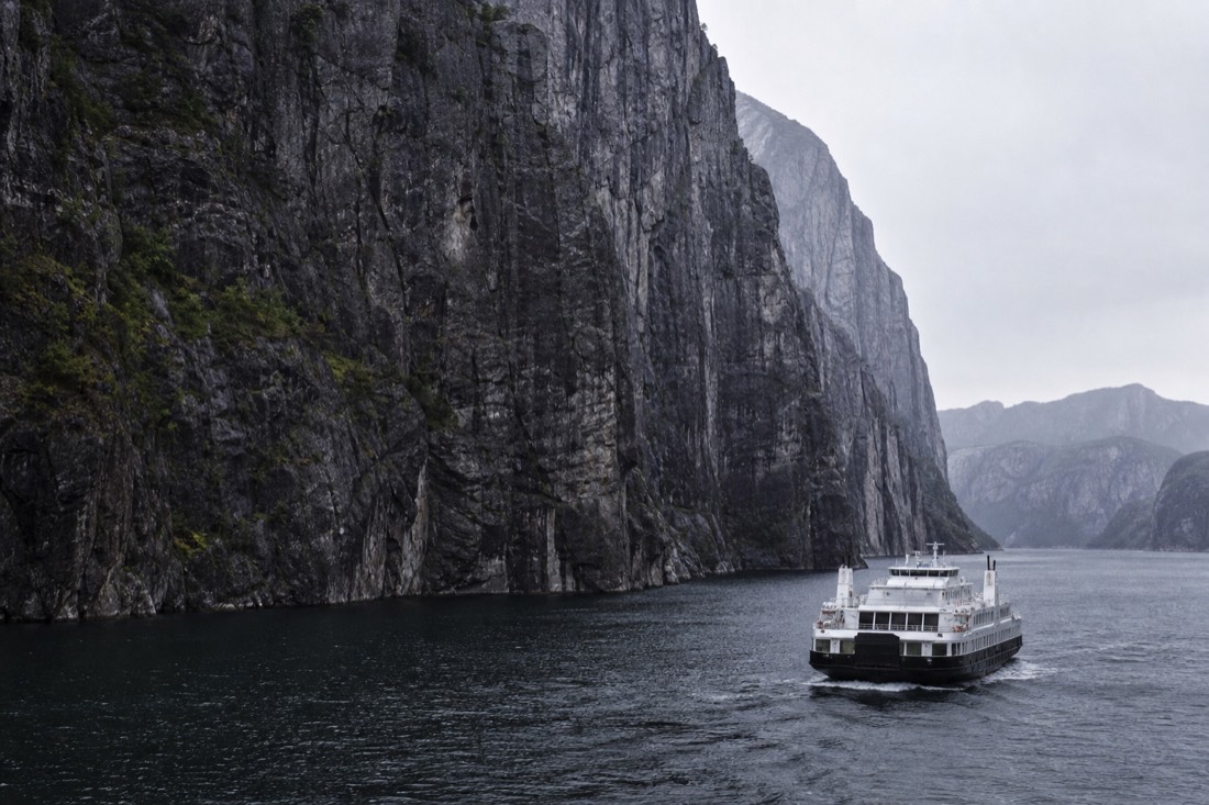 Passenger ferry crossing the Lysefjord with vertical grey cliff walls rising straight from dark water