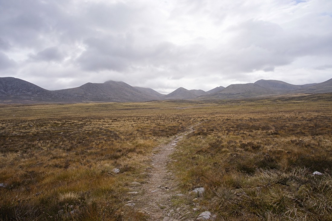 Worn footpath crossing open moorland toward distant mountains with no signage
