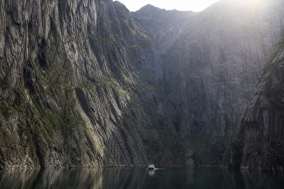 Sightseeing boat dwarfed by sheer fjord walls in a narrow inlet