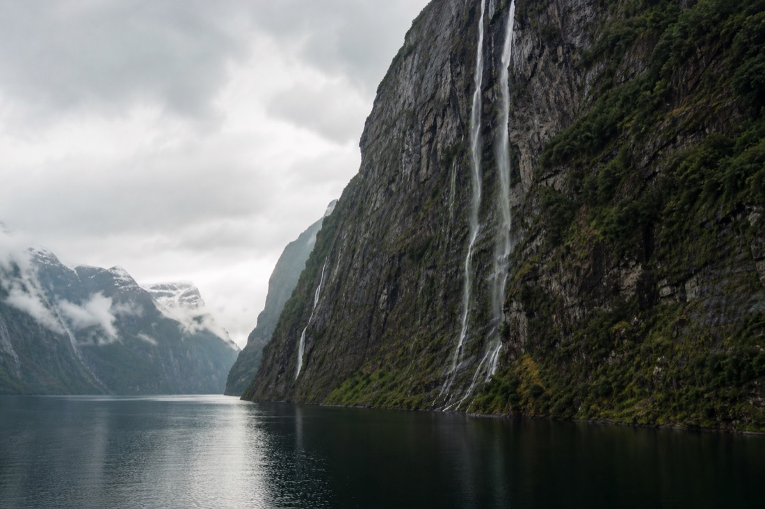 Narrow fjord arm with near-vertical walls and thin waterfalls falling to still water