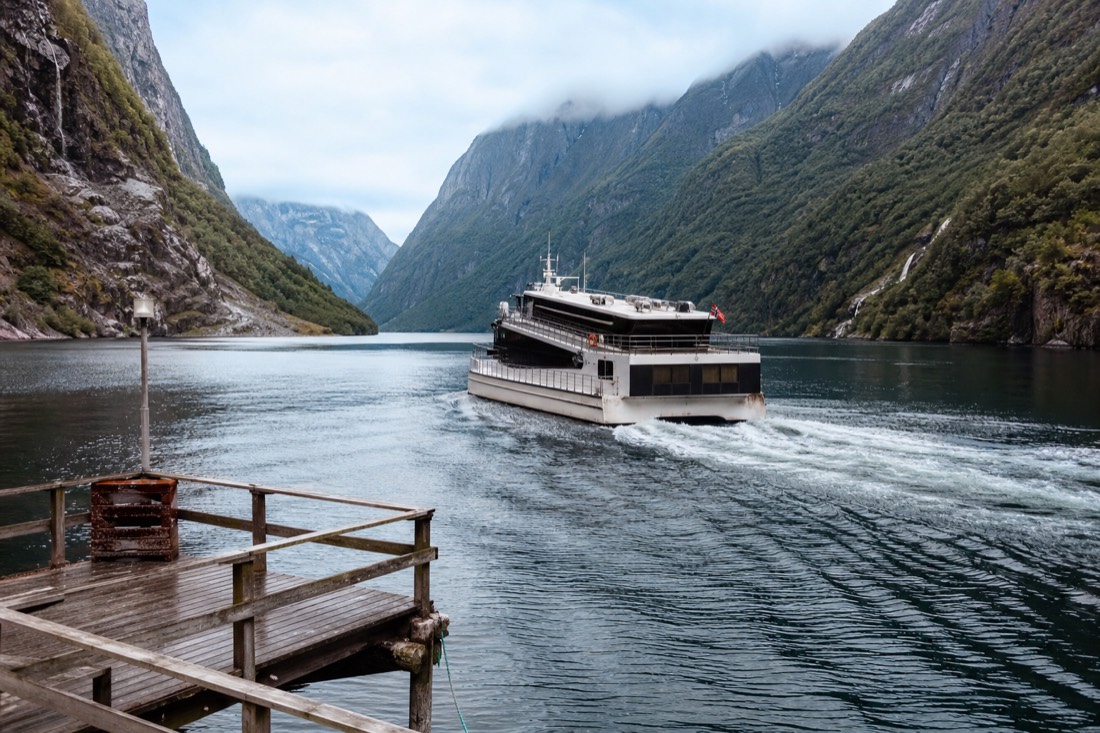 Express passenger boat pulling away from a small wooden jetty in a narrow fjord