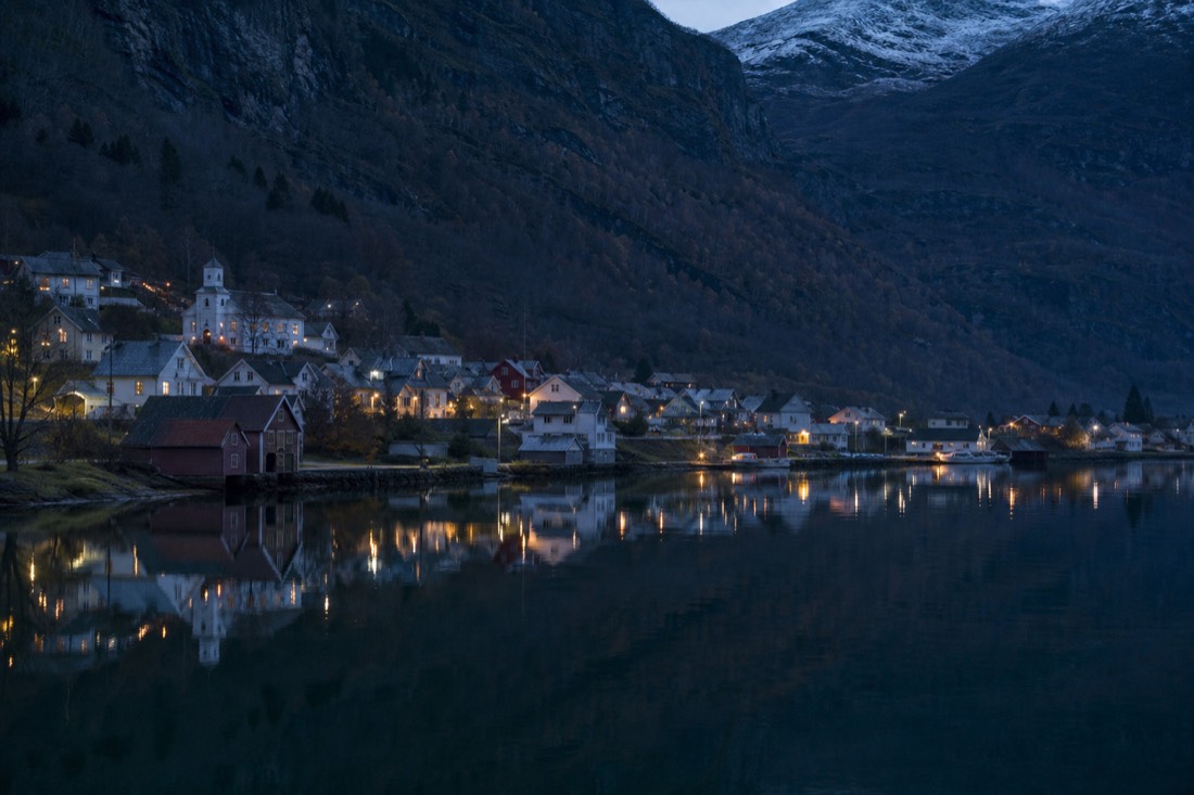 Quiet fjord village at dusk with lit windows reflected in still water