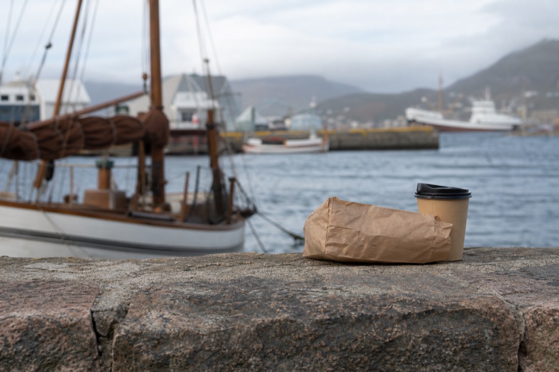 Paper bakery bag and takeaway coffee cup on a harbour wall overlooking moored boats