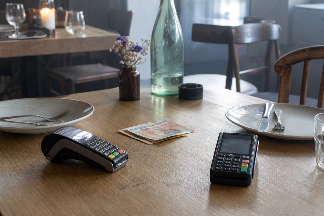 Restaurant table with two card terminals and a folded bill between empty plates
