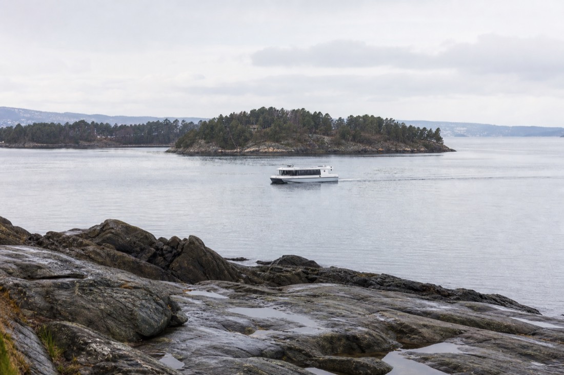 Quiet electric passenger boat gliding across a calm Oslofjord with wooded islands in the background