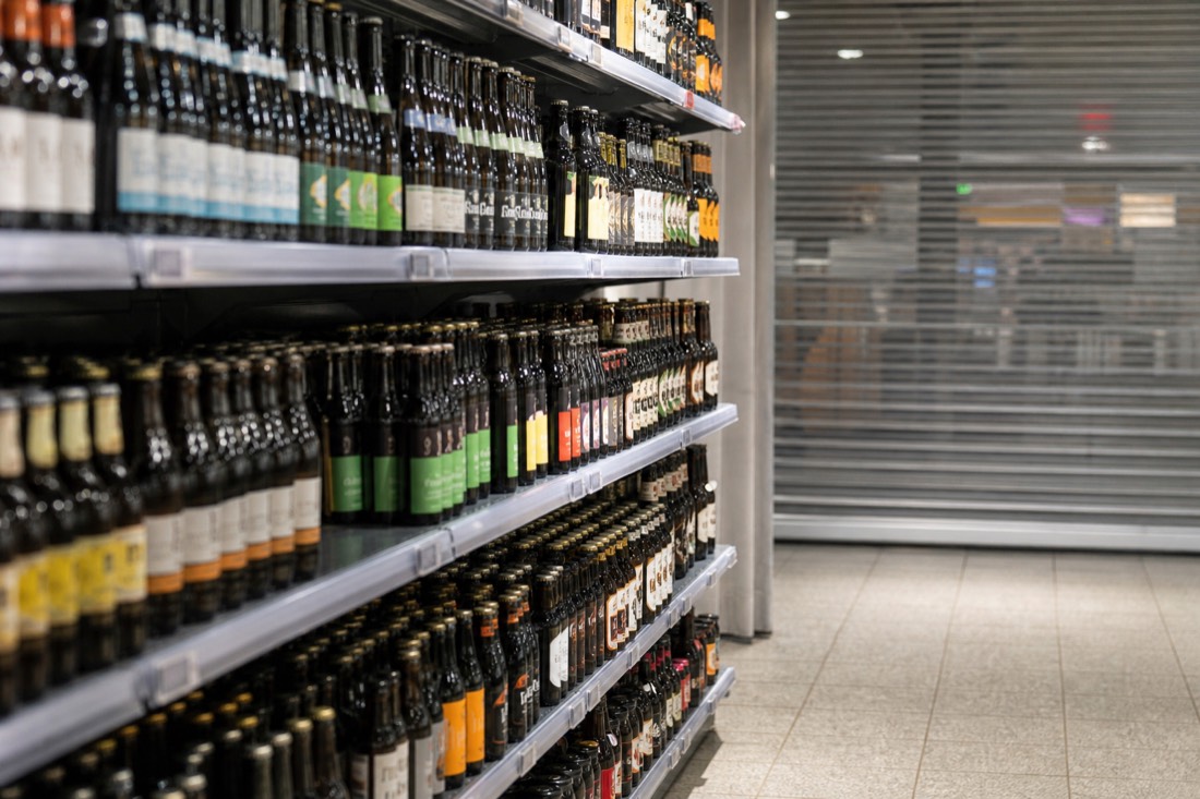 Supermarket shelf of bottled beer with a closed shutter section beyond