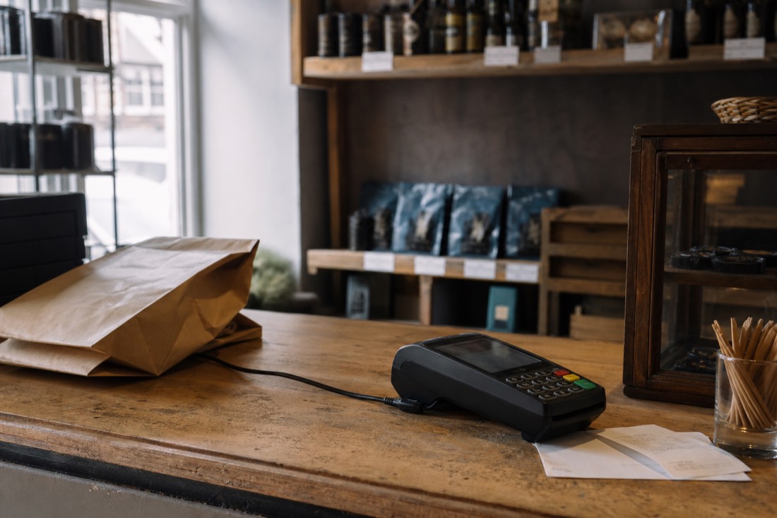 Shop counter with a card terminal and paper receipts beside a folded paper bag