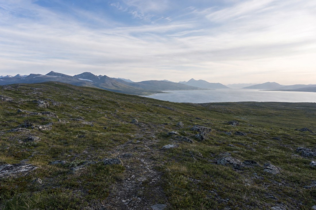 Open hillside with a faint path and no fences or signage stretching toward distant water