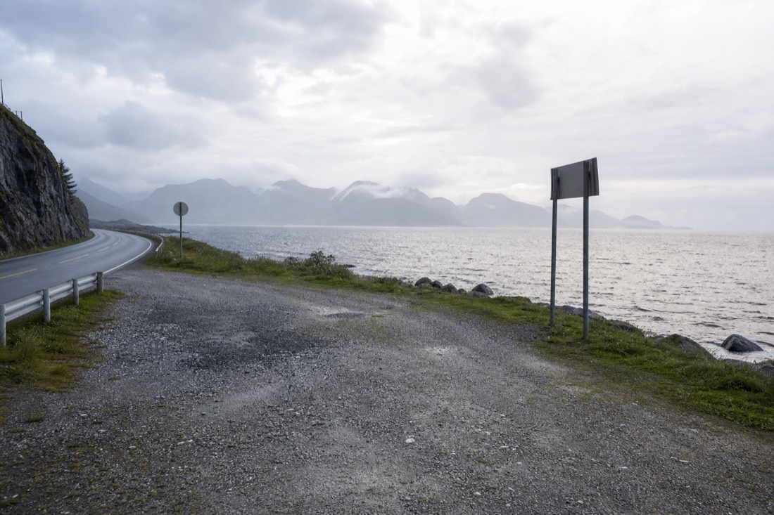 Gravel pull-in beside a Norwegian coastal road with a signpost and open sea beyond
