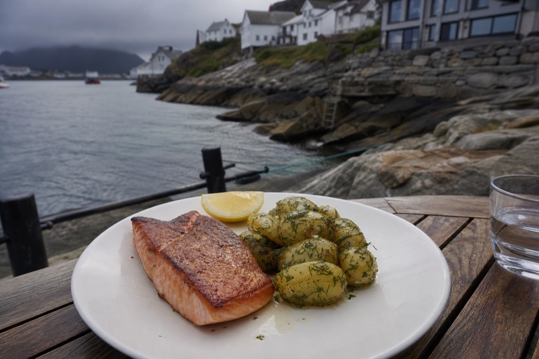 Plate of seared Norwegian salmon with dill potatoes and a lemon wedge in a harbourside restaurant