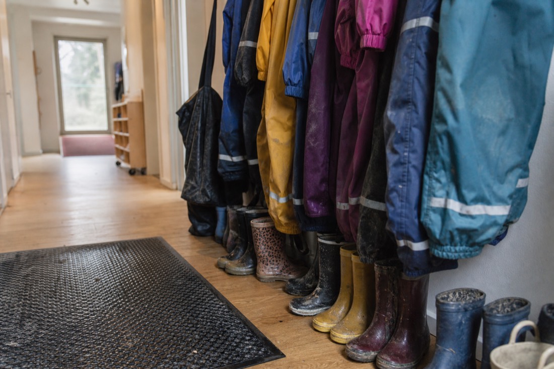 Children's waterproof suits and rubber boots lined up in a hallway beside a wet doormat