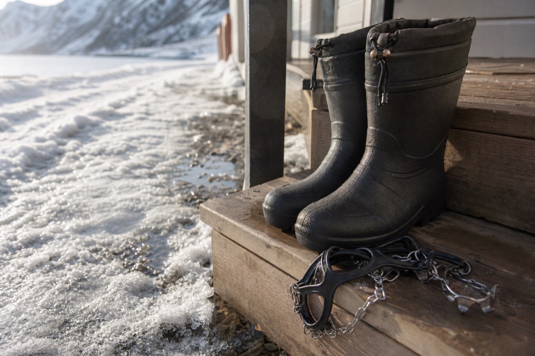Waterproof boots and clip-on ice grips on a wooden step beside packed snow