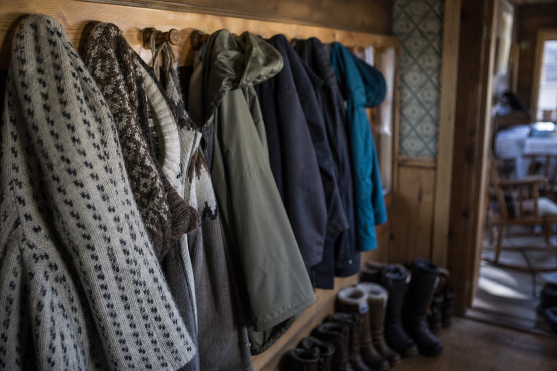 Wool sweaters and windproof shells hanging on pegs in a hallway with boots below