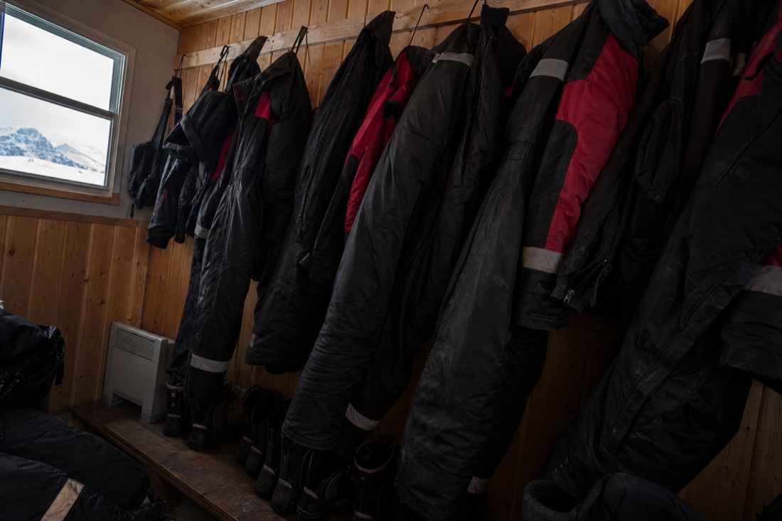 Thermal suits and boots hanging in a heated tour cabin with snow through the window
