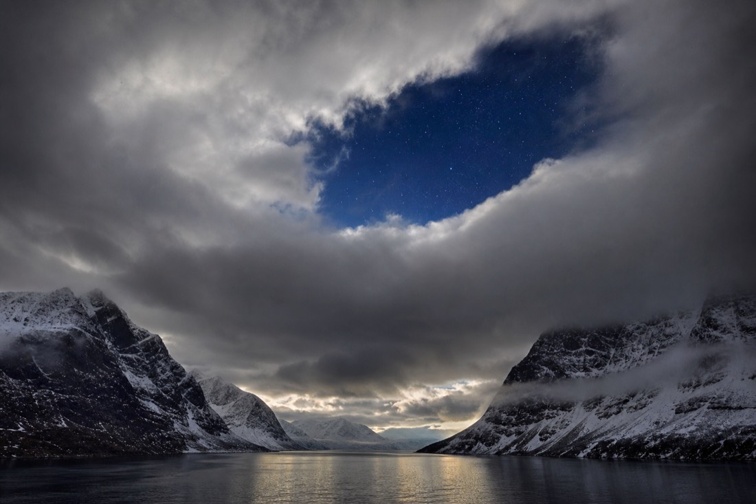 Break in heavy cloud over an Arctic fjord with a patch of clear starry sky showing