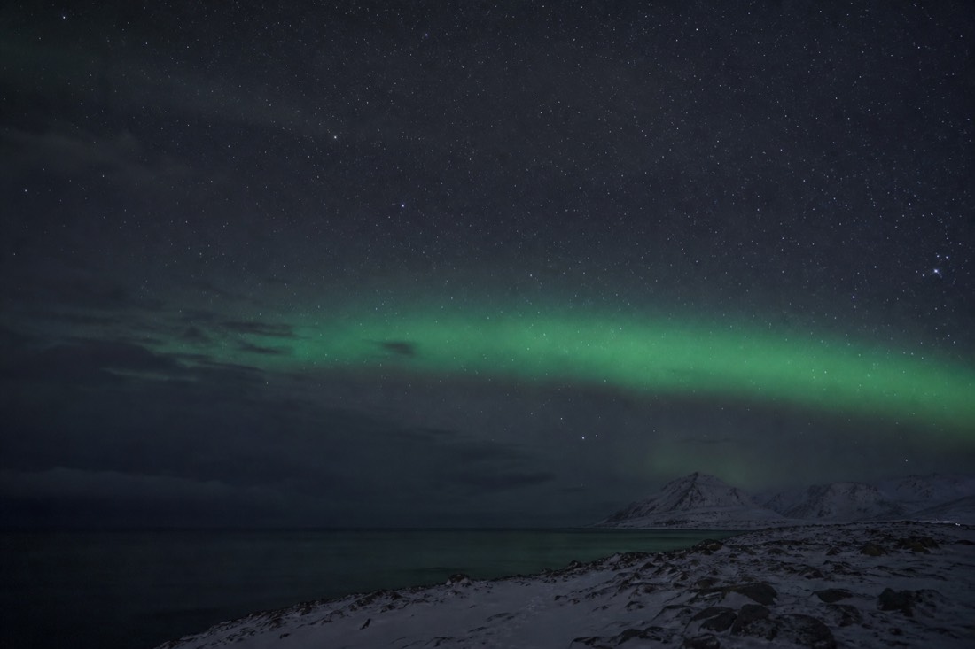 Faint pale green band across a starry night sky above a dark Arctic horizon