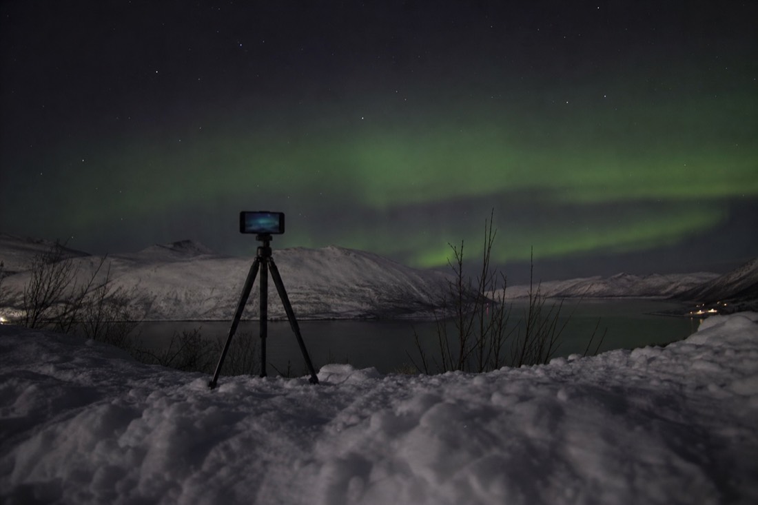 Small tripod set up on snow at night with an unreadable phone screen glowing faintly