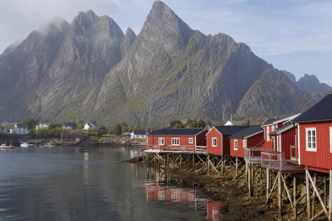 Red fishermen's cabins on stilts beside still water in a Lofoten village with granite peaks rising behind