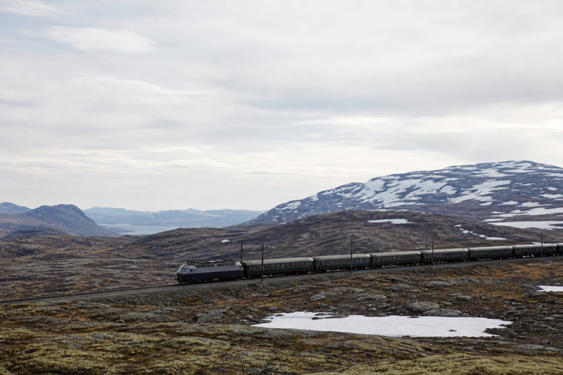 Long-distance train crossing a bare high plateau with snow patches under a wide sky