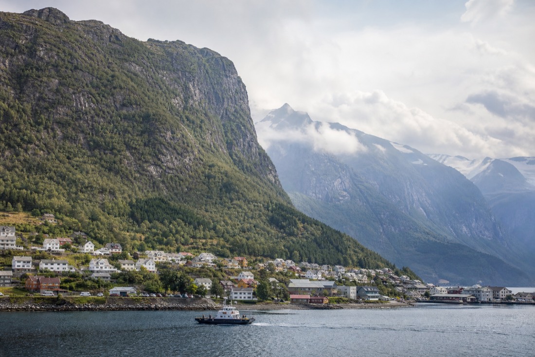 Wide view of a fjord village with mountains behind and a small ferry crossing the water