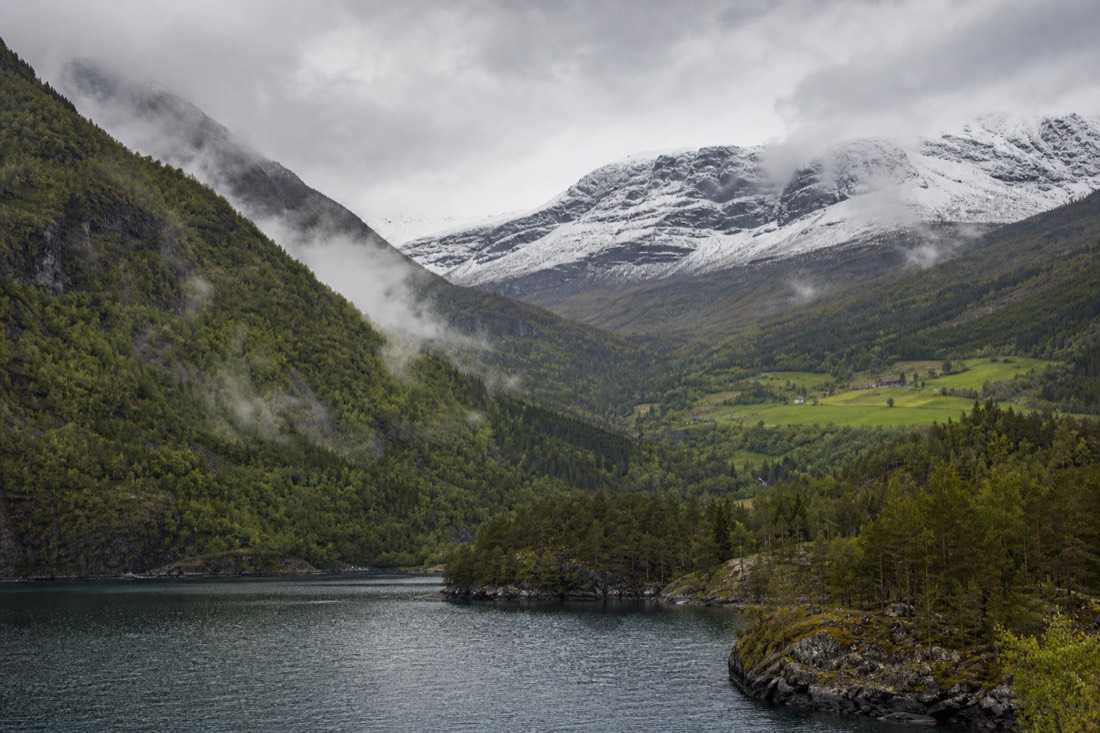 Split landscape of a green summer fjord valley meeting a snow-covered Arctic shoreline