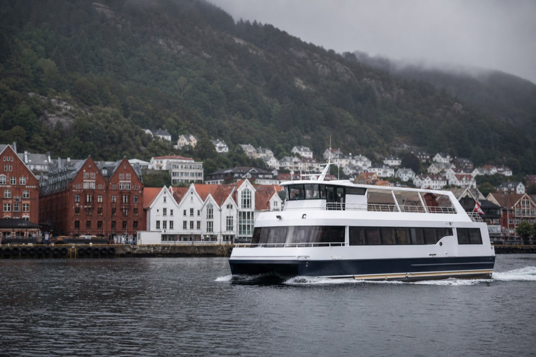 Fjord cruise boat leaving Bergen harbour quay with wooden warehouses behind