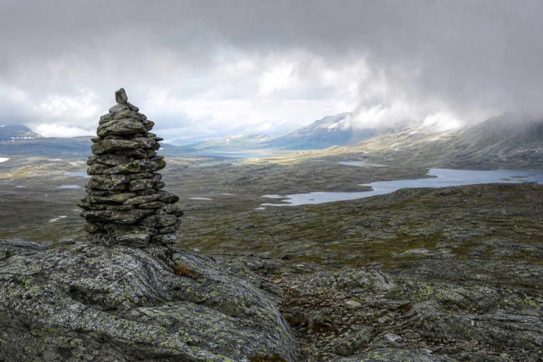 Trail marker cairn on bare rock with cloud moving across a Norwegian plateau