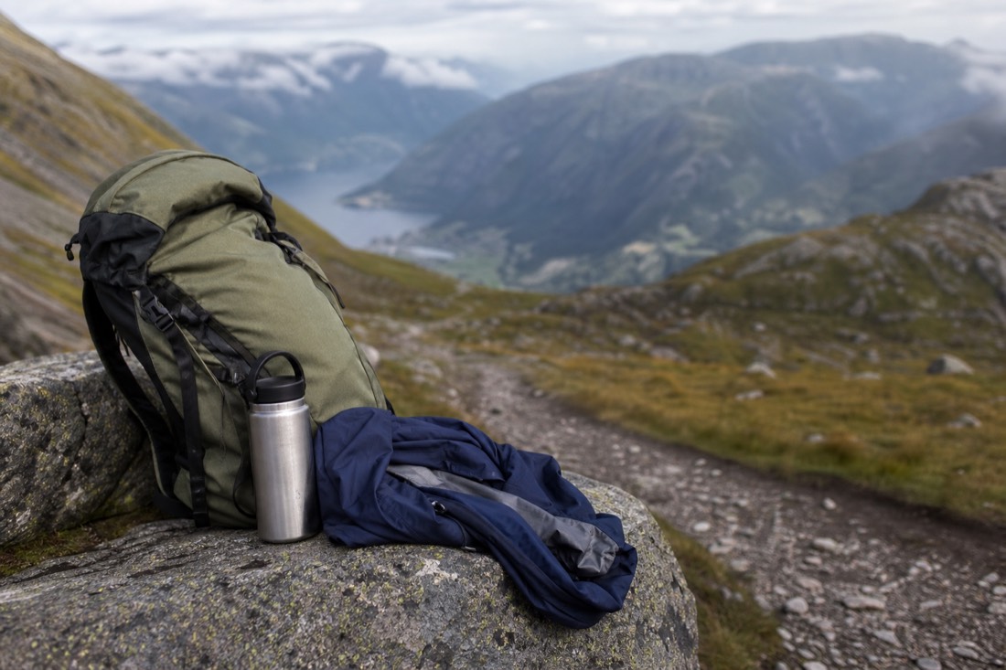 Hiking pack, water bottle and waterproof jacket on a rock beside a mountain trail