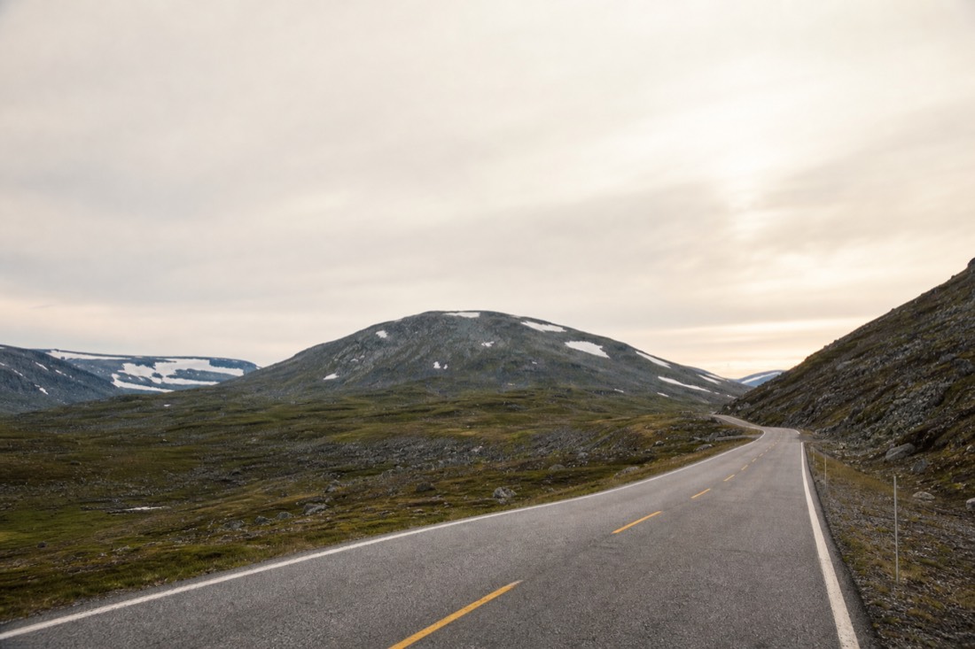 Long empty road curving between low Arctic mountains under a wide pale sky in northern Norway