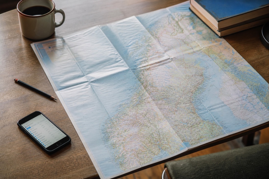 Map spread on a table with a coffee cup, pencil and a phone showing a train timetable