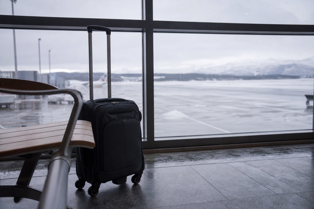 Compact carry-on bag beside a bench at a Norwegian airport gate with a runway visible outside