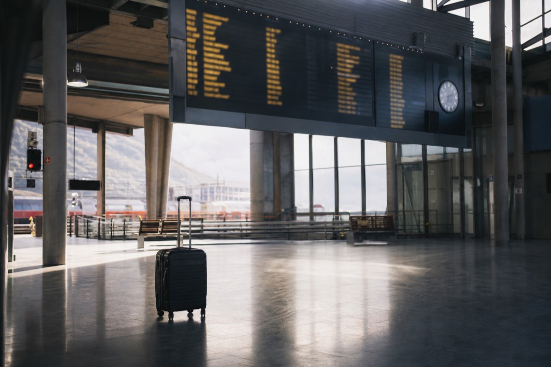 Departure board and a single suitcase in a quiet Norwegian station concourse with morning light on the floor
