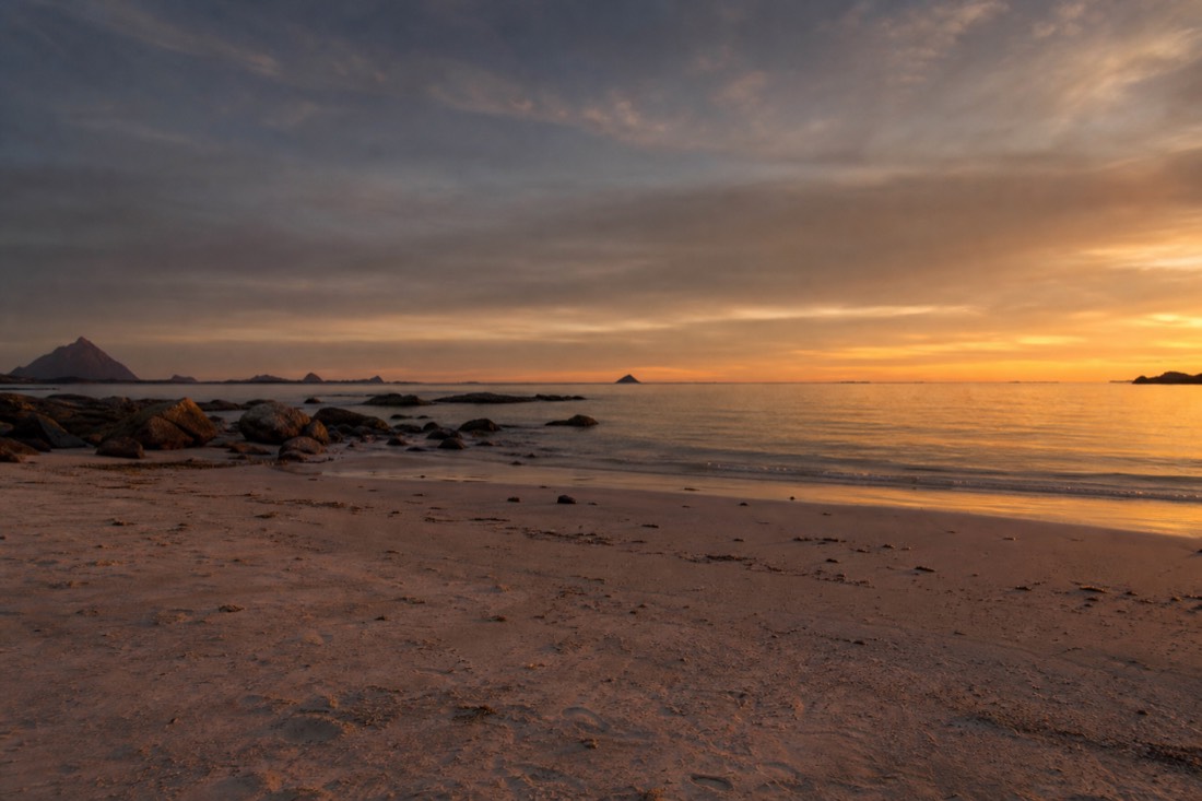 Empty beach in northern Norway at night with warm low sunlight on pale sand and calm sea