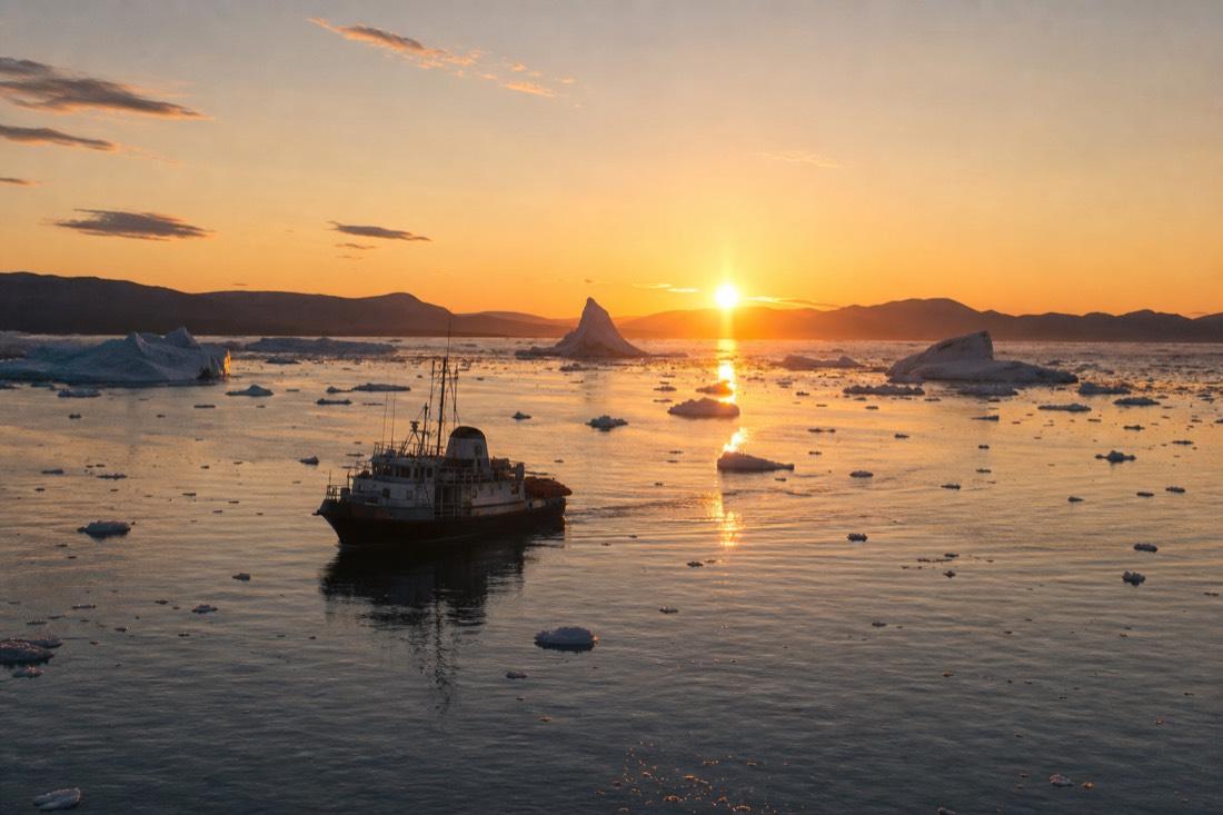 Small tour boat on calm Arctic water late at night with the sun low and golden on the horizon