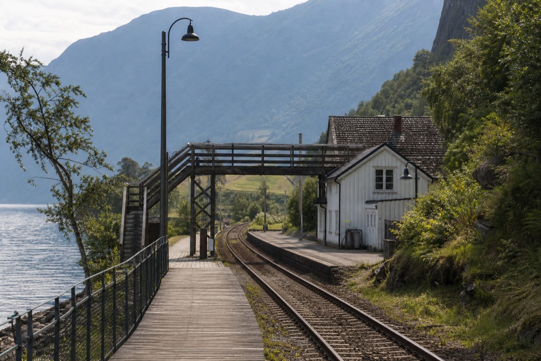 Small fjord-side village station with a wooden platform and a footbridge over the tracks