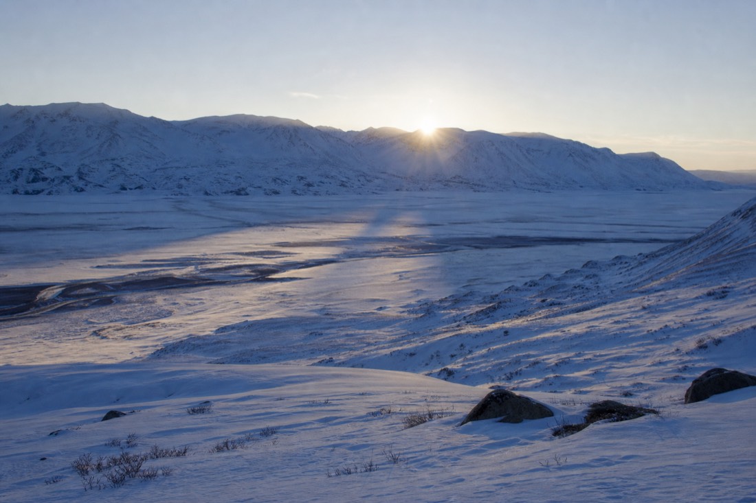 Low winter sun barely clearing a snowy ridge, casting long blue shadows across a frozen valley