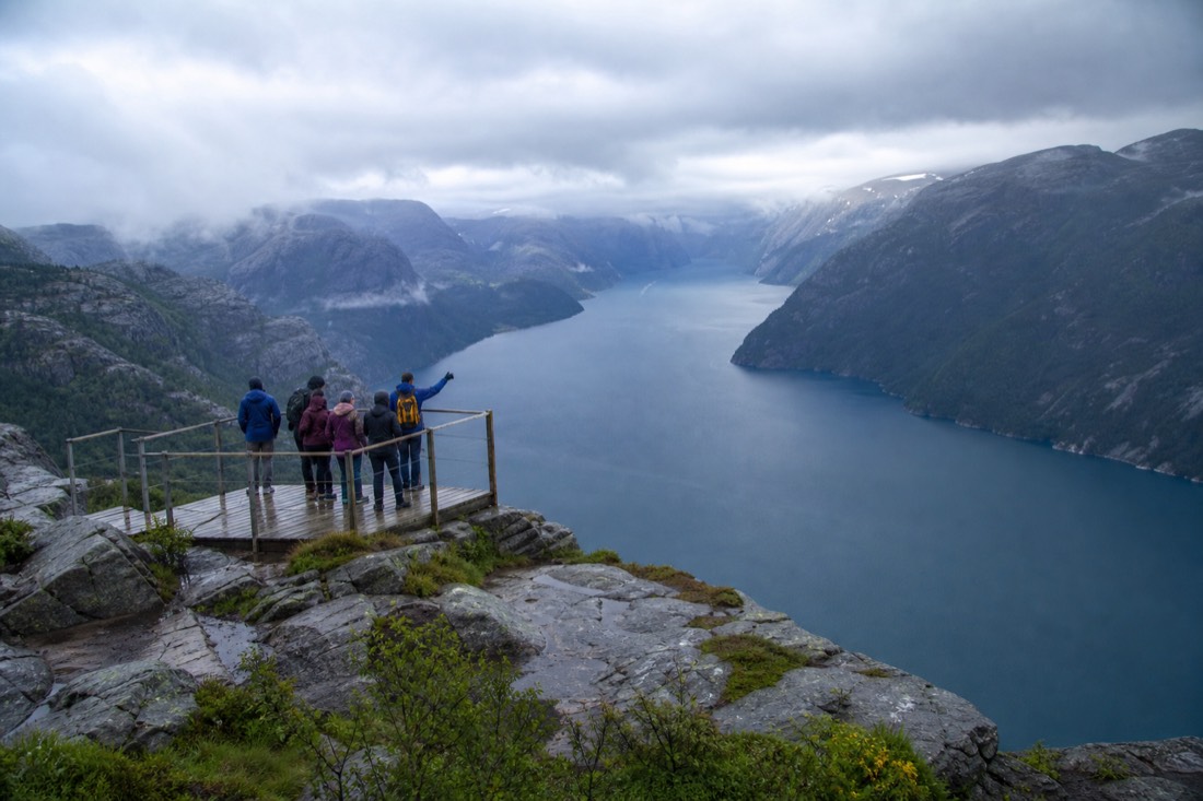 Small group of travellers with a guide on a viewing platform above a deep blue Norwegian fjord