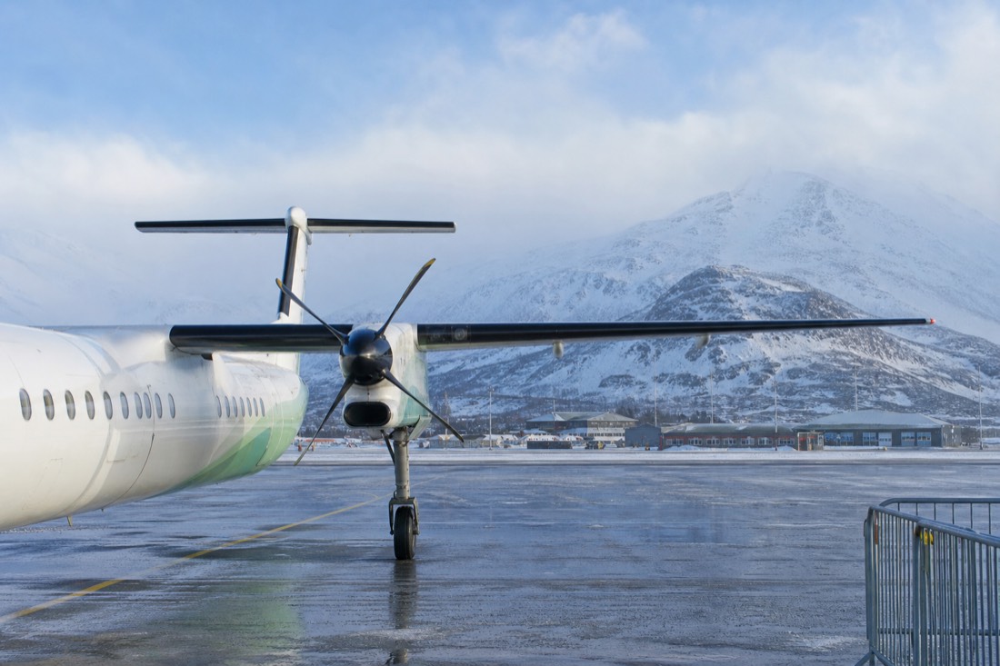 Small regional aircraft on a snowy northern Norwegian apron with mountains behind the terminal