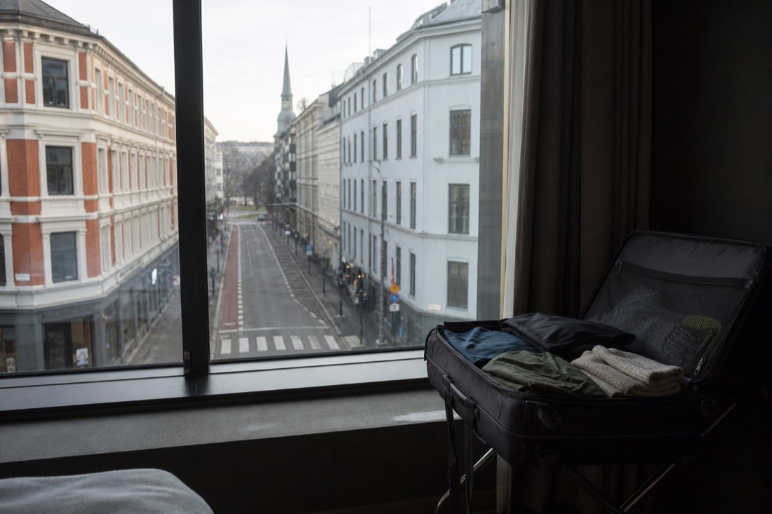 Hotel window view over an Oslo street early in the morning with a suitcase open on a luggage rack
