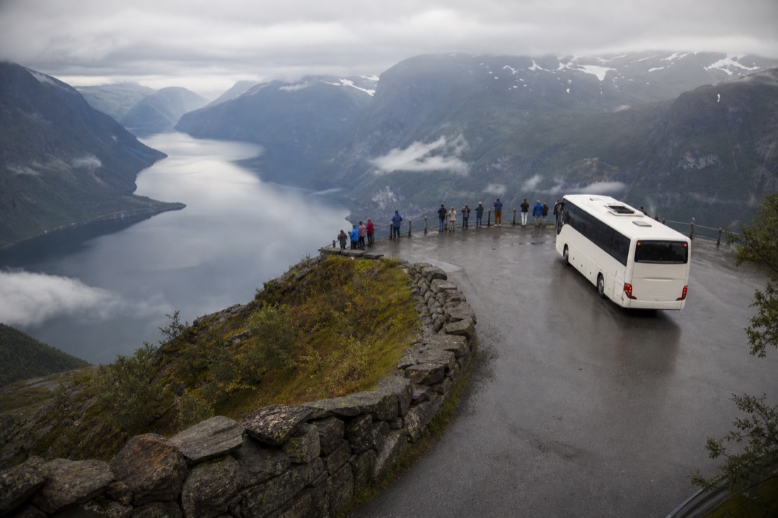 Coach parked at a mountain viewpoint above a fjord with travellers at the railing looking down