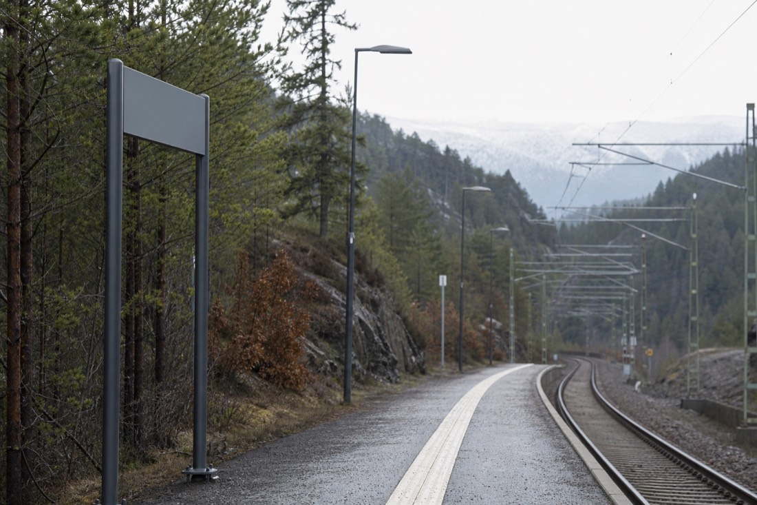 Railway platform sign post at a northern European station with tracks curving away into forest