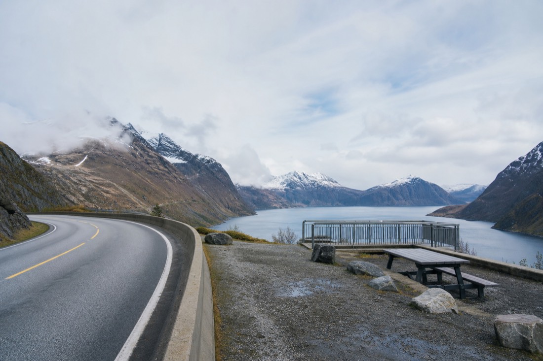 Empty scenic road curving along a fjord edge with a rest area and viewpoint railing