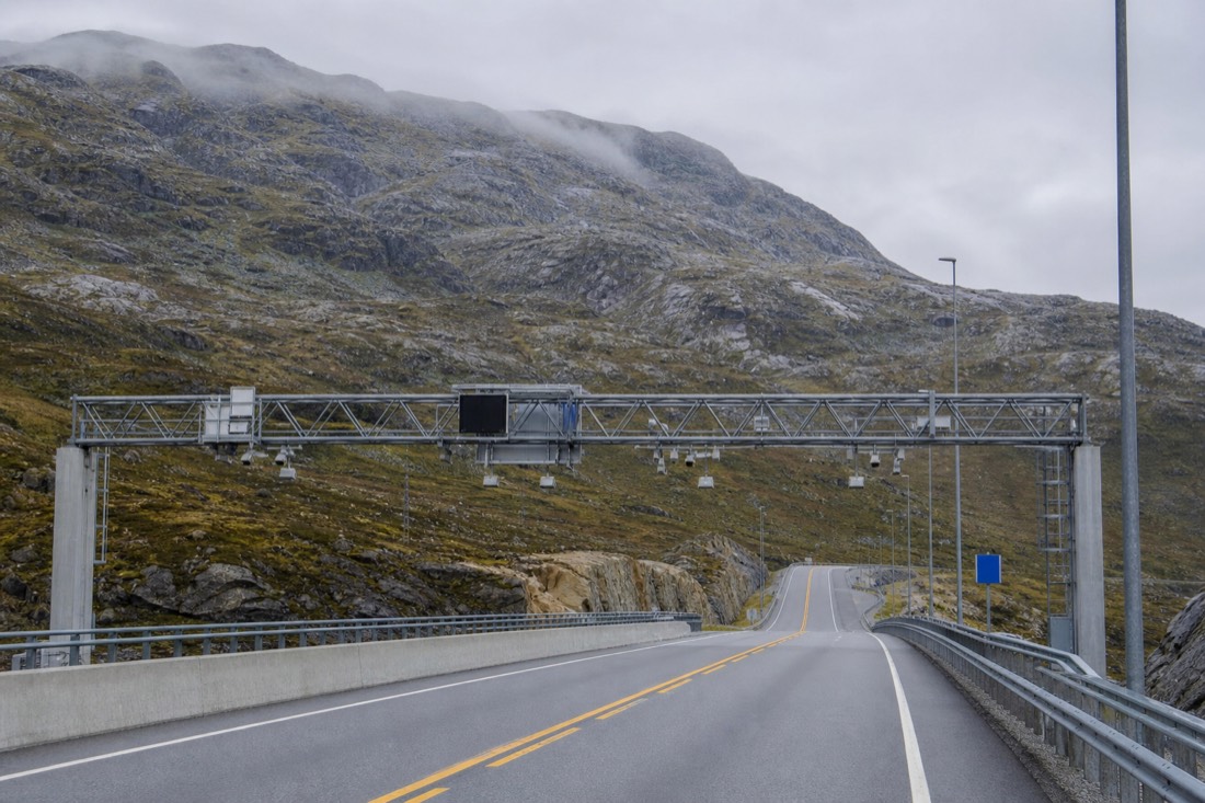 Automatic toll gantry over an empty Norwegian road with mountains behind