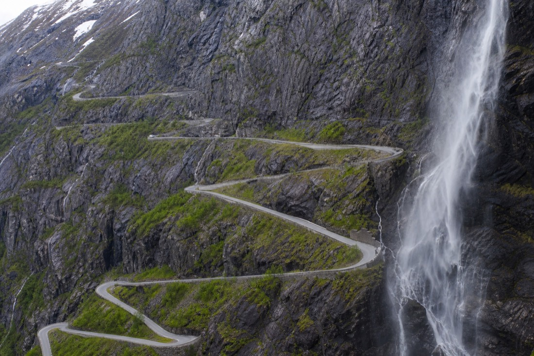Hairpin mountain road switchbacking up a steep rock face with a waterfall alongside