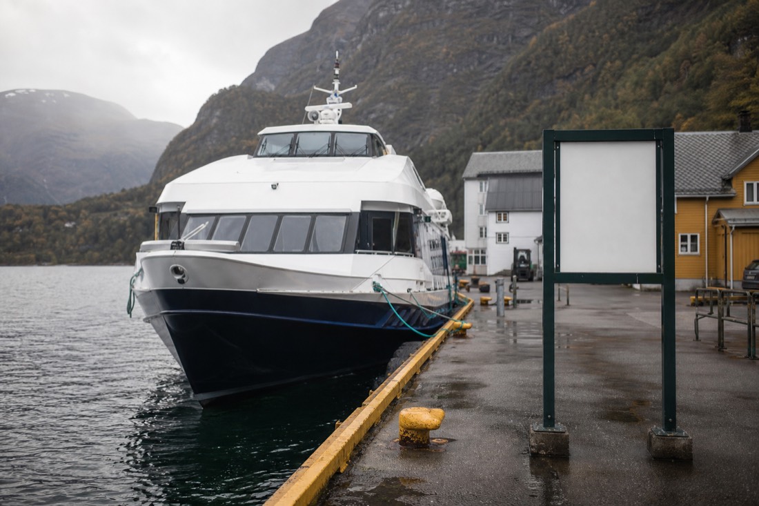 Express passenger boat moored at a small fjord village jetty with a timetable board